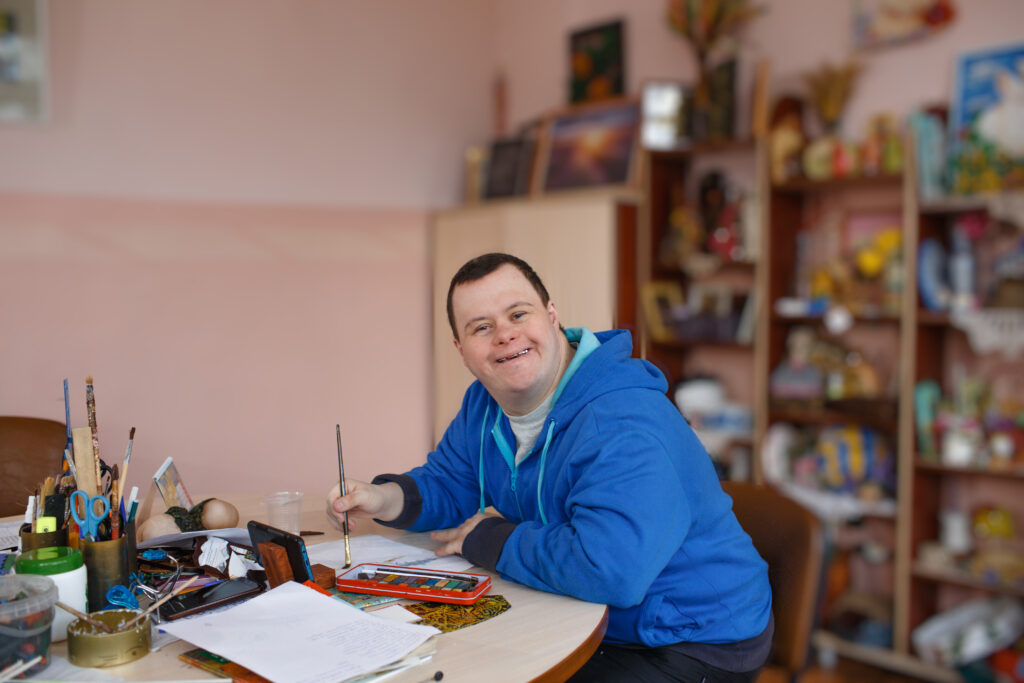 Man with down syndrome is engaged in drawing in a workshop.